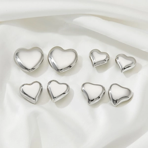 Eight minimalist silver stainless steel heart earrings arranged on white silk fabric