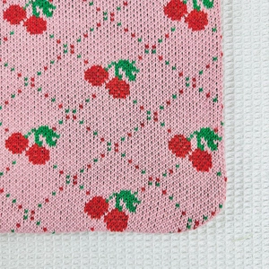Close-up of pink knit fabric with red cherry patterns and detailed woven texture
