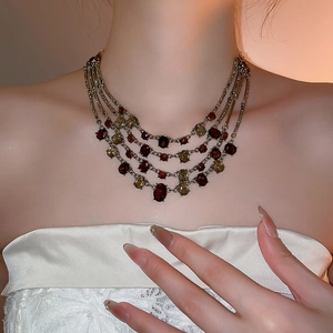 Detail of vintage layered necklace with red and green gems on female model