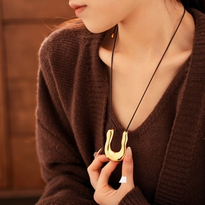 Chic U-shape gold pendant necklace with black cord chain worn on a brown knit sweater