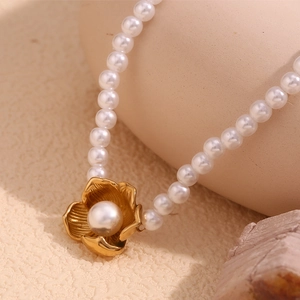 Detail of 18K gold plated flower pendant with central pearl on a pearl necklace chain