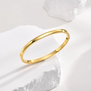 Minimalist gold stainless steel bangle with polished mirror finish on white stone stand