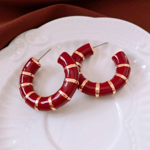 Detailed view of red and gold striped C-shape hoop earrings on a white embossed plate