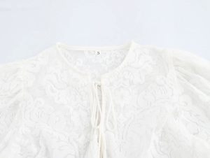 Close-up of white lace cardigan showing floral patterns and tassel drawstring ties