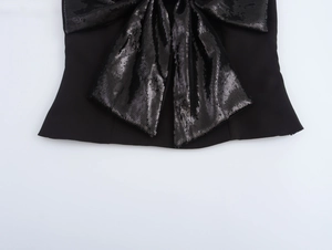 Détail d'un haut noir orné d'un grand nœud 3D en paillettes sur tissu mat et élégant