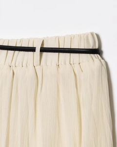Détail de la jupe midi plissée beige élégante avec une fine ceinture noire à la taille
