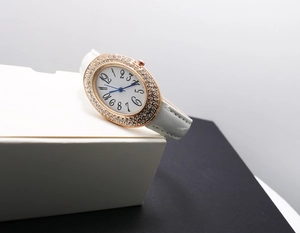 Detail of oval rose gold watch case with rhinestone bezel and white leather strap