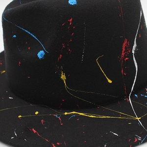 Detailed close-up of colorful paint splatter on a black wool fedora hat's texture
