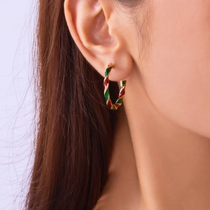 Detail of red and green spiral enamel twist hoop earring on female model's ear