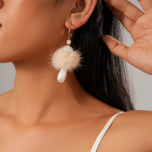 Detail view of elegant drop earrings with beige fur pompom and white pearl on model