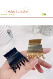 Detail showing polished gold and glossy black alloy hair claws on a minimalist background