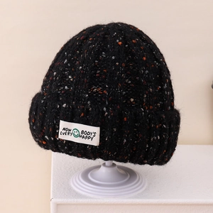 Detailed knit texture of black speckled beanie with happy face slogan patch