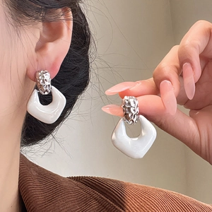 Detail of silver twisted metal and white enamel U-shaped drop earrings on model