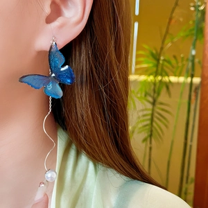 Detail of blue butterfly drop earring with silver wave chain and pearl on model