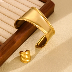 Close-up of polished gold-plated cuff bracelet and spiral wave ring set on a jewelry box