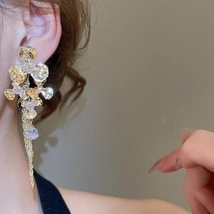 Close-up of dangling flower earrings with teardrop crystals and gold tassels on a model