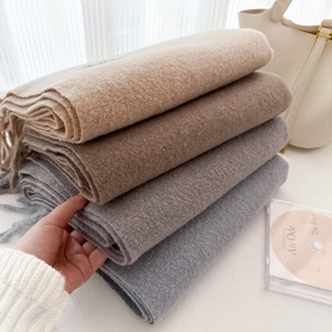 Stack of thick solid color wool scarves with tassels in beige, camel and grey tones