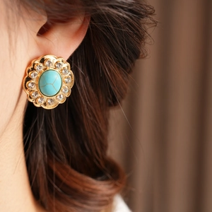 Gros plan d'une boucle d'oreille fleur dorée avec turquoise et strass portée par un mannequin
