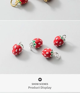 Macro detail of strawberry jewelry charms with red enamel and green leaf accents