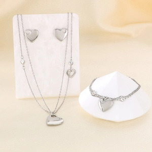 Three-piece silver heart jewelry set featuring layered necklace, bracelet and stud earrings