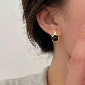 Close-up of golden teardrop earring with black agate gemstone on model ear