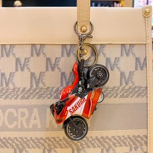 Red pull-back motorcycle keychain pendant hanging on a beige tote bag for decoration