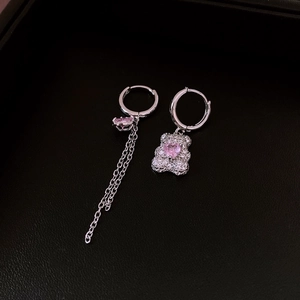 Detail of silver bear earrings with pink heart stones and tassel chain on black background