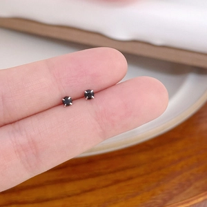 Macro view of 4-prong set black mini zircon stud earrings held between fingers