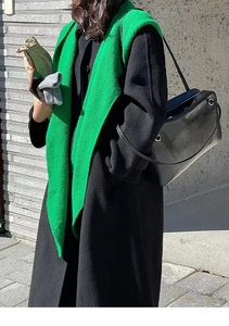Detail shot of a lime green knitted scarf draped over a classic black wool coat for winter