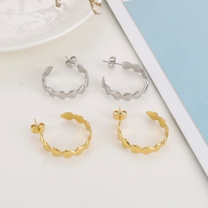 Detail of gold and silver heart-shaped hoop earrings with interlocking pattern on white ceramic
