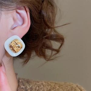 Close-up of vintage square stud earrings with 18k gold plating and white enamel finish