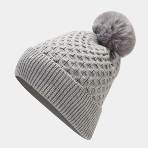 Detailed view of gray knit beanie with fluffy faux fur pompom and honeycomb texture