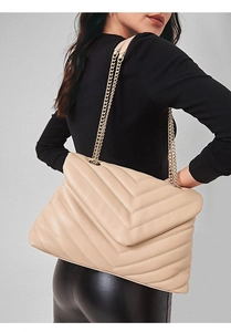 Detail shot of apricot quilted tote bag with gold chain strap on model's shoulder
