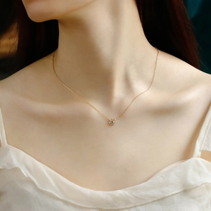 Detailed close-up of a 14K gold daisy flower pendant with green zircon on a model neck
