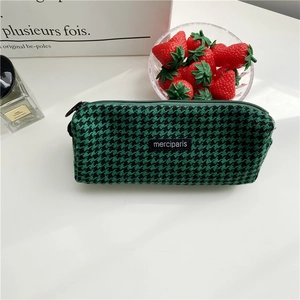 Detail of green houndstooth fabric pencil case with black zipper and woven brand tag
