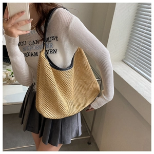 Beige woven straw shoulder bag with black trim worn by a model in a casual summer outfit