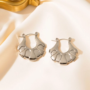 Detail of silver-toned wave fan-shaped hoop earrings on soft cream silk fabric
