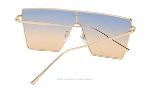 Detail of oversized square sunglasses with gold metal frame and blue-orange gradient lens