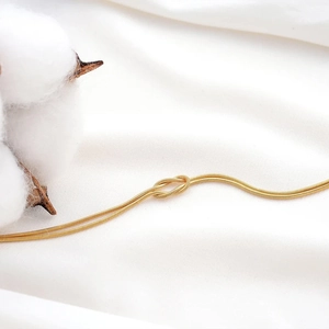 Detailed macro view of a gold-tone snake chain bracelet featuring a polished love knot
