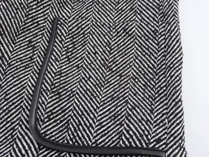 Close-up of black and white herringbone tweed fabric with black leather trim detail