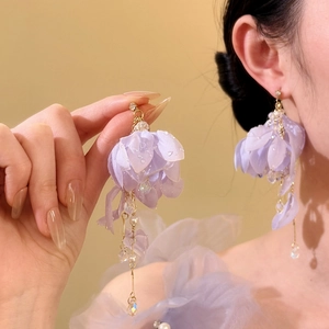 Close-up detail of purple fabric flower earrings with pearls and water droplet accents.