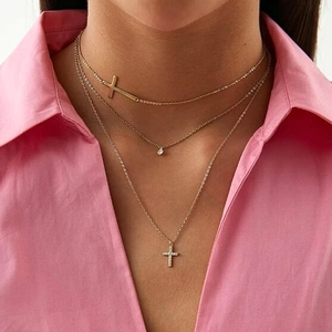 Detailed view of layered gold cross necklaces with sparkling zircon pendants on model