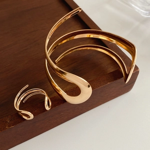 Primo piano del bracciale rigido dorato lucido e dell'anello coordinato su legno