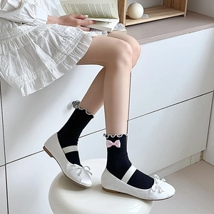 Close-up of black JK socks with white ruffle trim and pink bows paired with Mary Janes