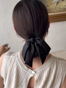 Rear view of model wearing a large black satin bow hair clip for a low bun hairstyle