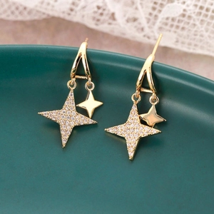 Macro shot of gold star drop earrings with sparkling cubic zirconia on green ceramic