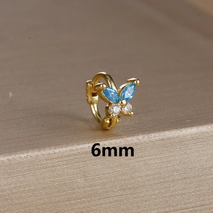 Macro detail of 6mm golden butterfly cartilage hoop with blue and clear zircon stones