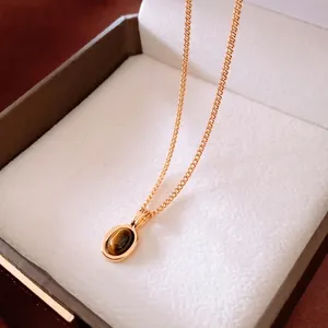 24K vergoldete Halskette mit Kreuzanhänger und ovalem Tigerauge-Stein auf Schmuckbox