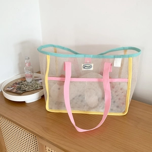 Detail of a mesh beach bag featuring pink handles and colorful trim on a wooden cabinet