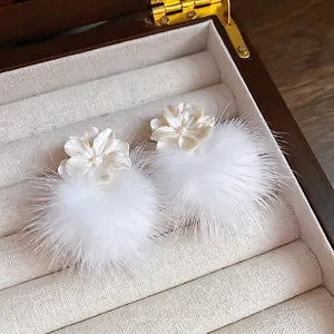 Boucles d'oreilles fleurs blanches avec pompons en peluche sur un coffret en velours beige